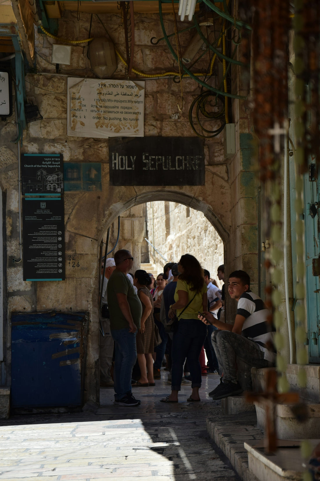 People gather under an archway labeled holy sepulchre sign.